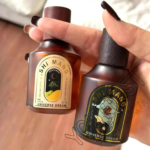 Two SHIMANG amber perfume spray bottles with dark cork caps held in hands